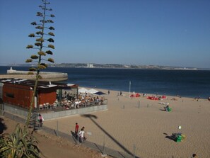 A beach with a building that has outdoor seating and umbrellas. - Wonderful Paço D' Arcos (Paço de Arcos)