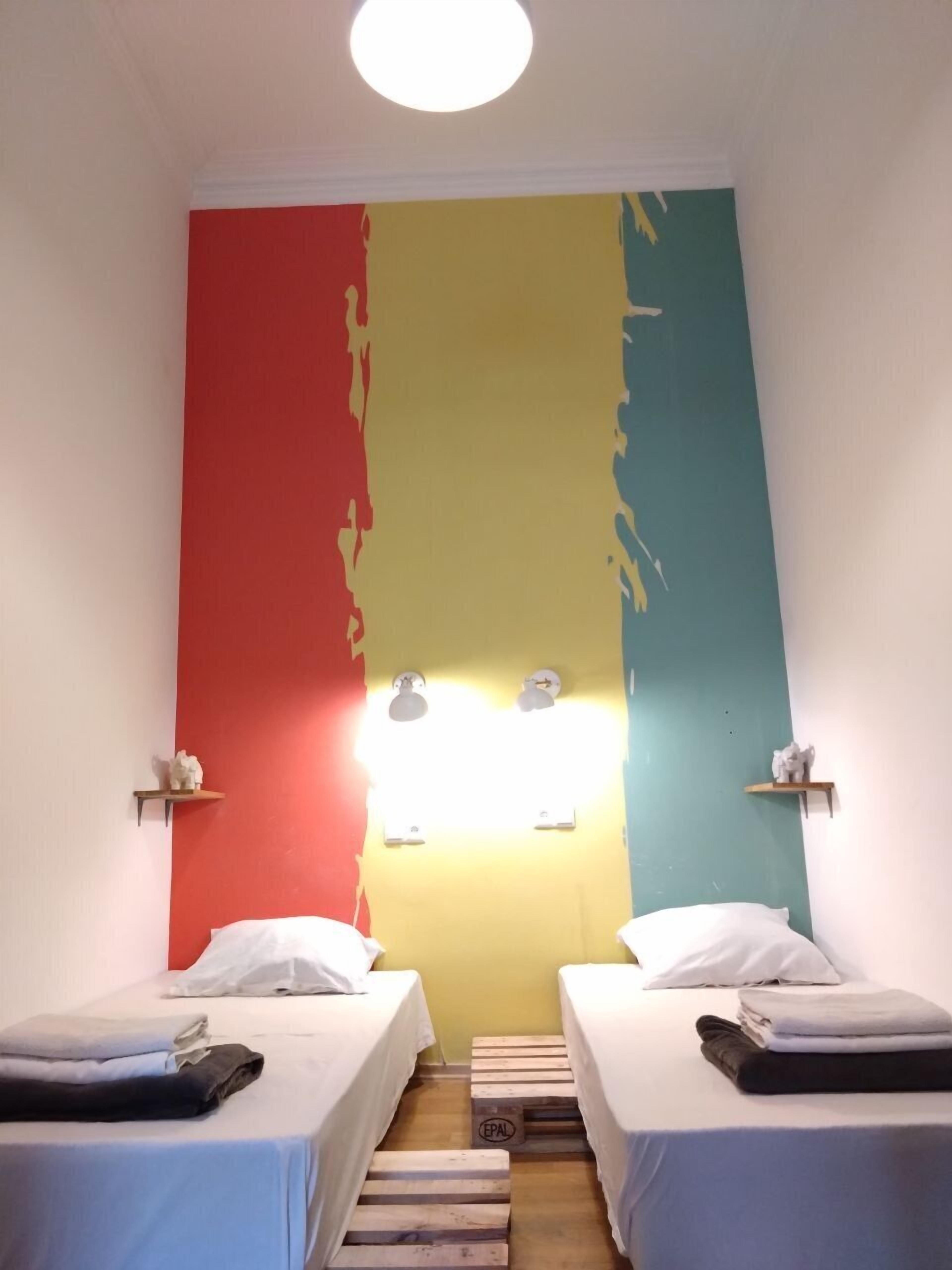 Ein Zimmer mit zwei Betten, einer Wand mit farbigem Dekor und einer Leuchte über den Betten.