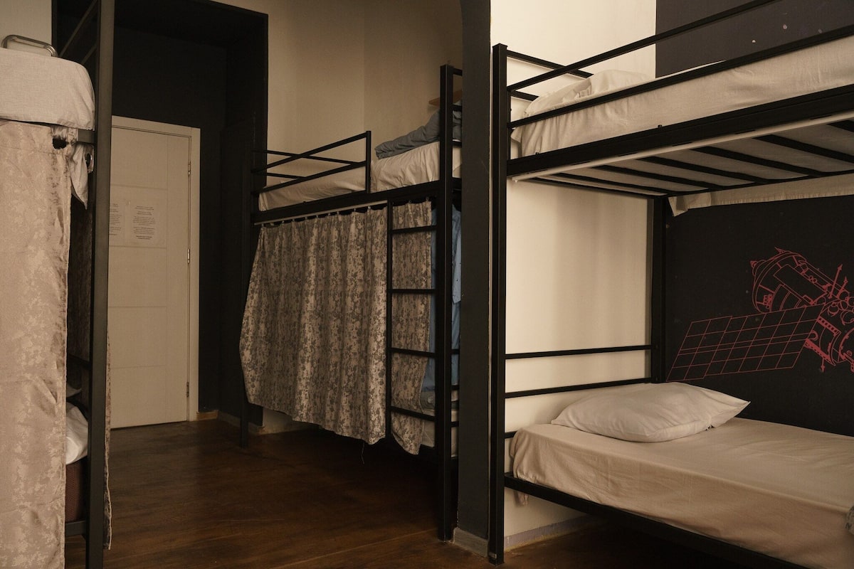 A dormitory room with bunk beds, a door with a notice, and a patterned curtain.