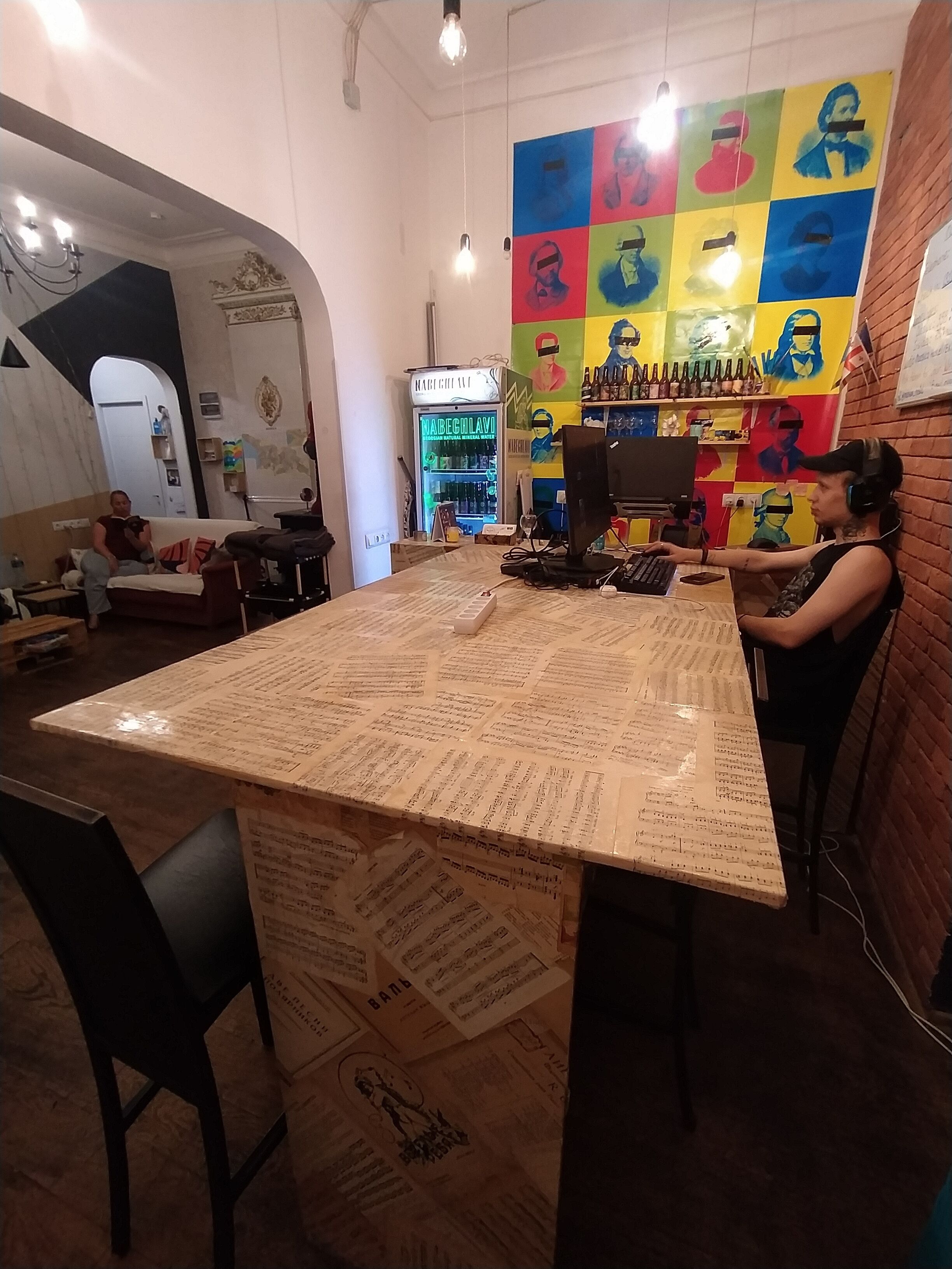 Una zona de bar con un letrero de neón, un mural colorido y una mesa cubierta de hojas impresas.
