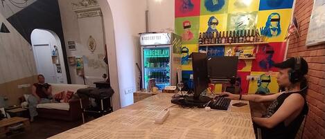 Una zona de bar con un letrero de neón, un mural colorido y una mesa cubierta de hojas impresas.