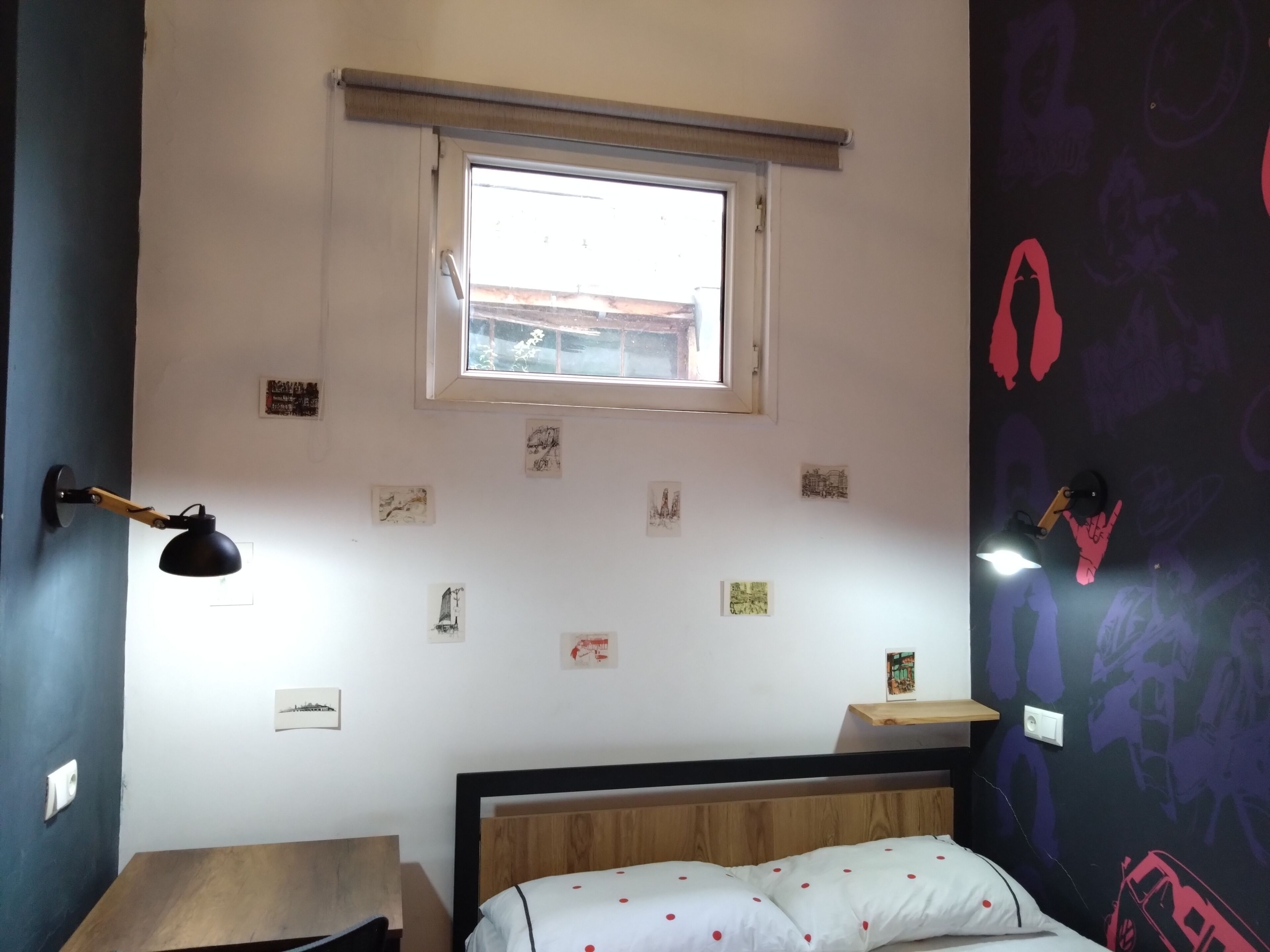 A bedroom with a bed, a desk, a window, and various wall decorations.