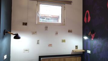 A bedroom with a bed, a desk, a window, and various wall decorations.