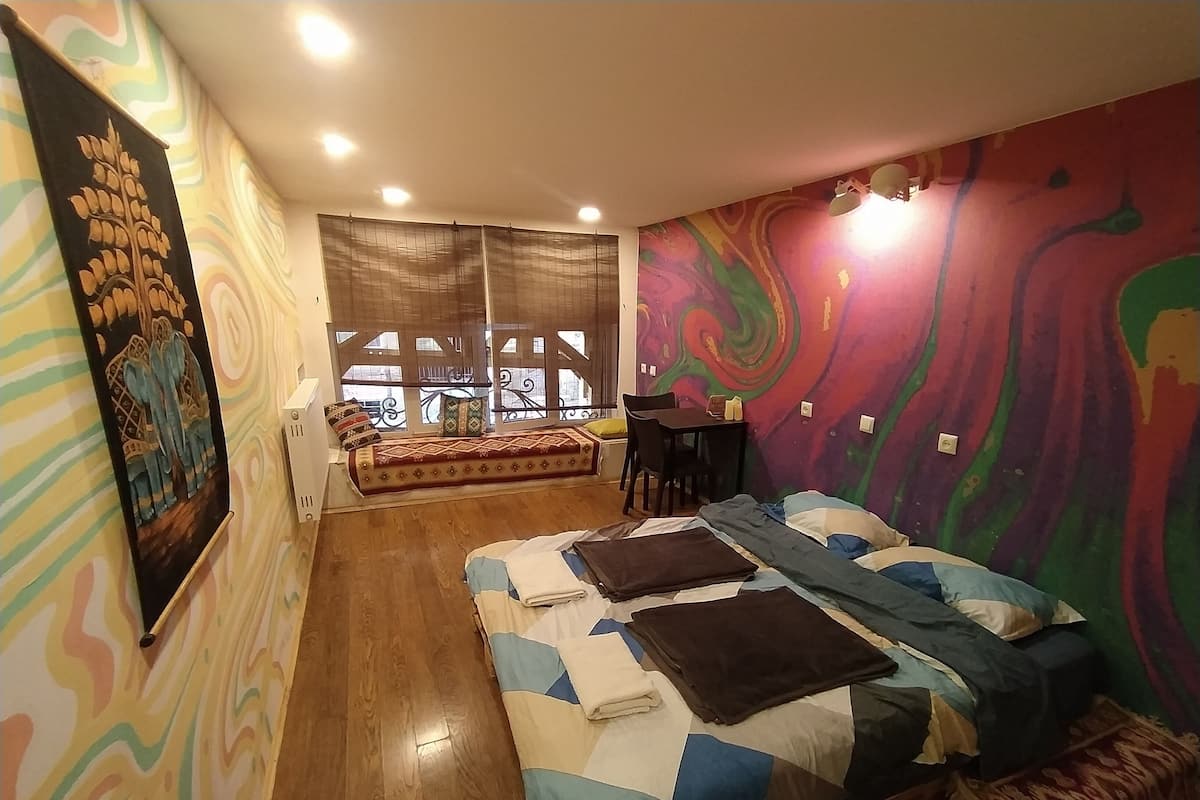 A bedroom with a bed, a sofa, a small table, and a window with a view.
