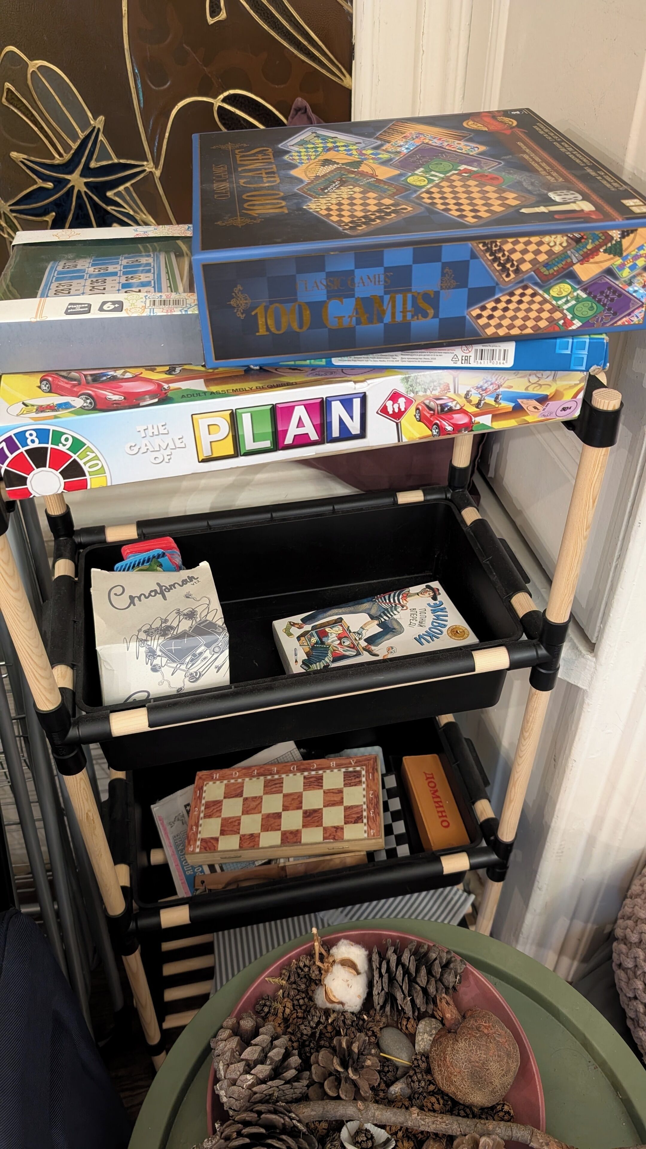 Una estantería de madera con juegos de mesa, incluyendo 'Plan' y '100 Games'.