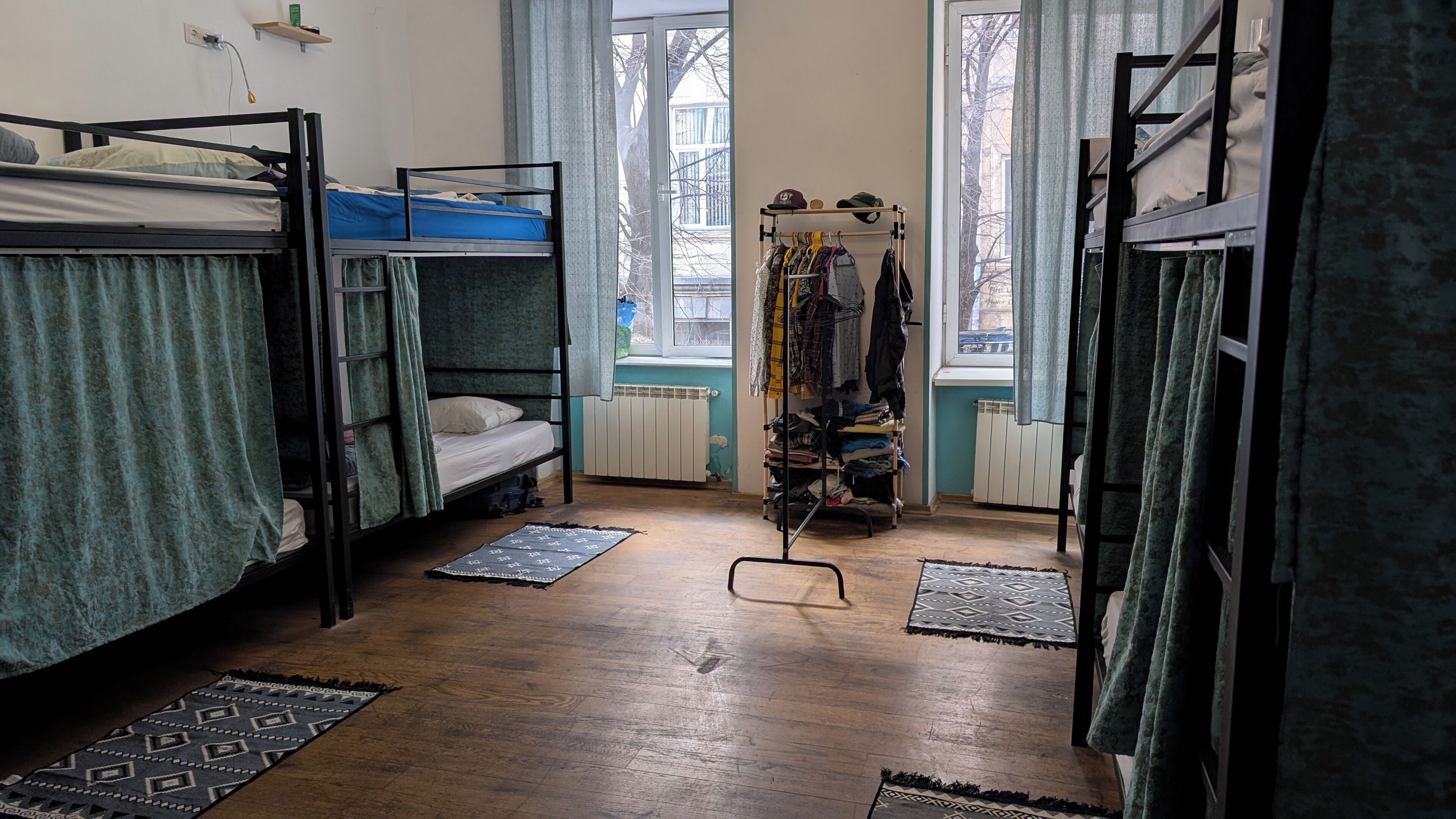 Un dormitorio con literas, un perchero y una ventana con vistas a edificios.