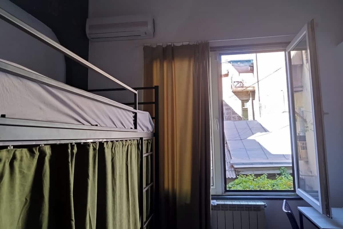 A dormitory room with bunk beds, a window with curtains, and an air conditioning unit on the wall.