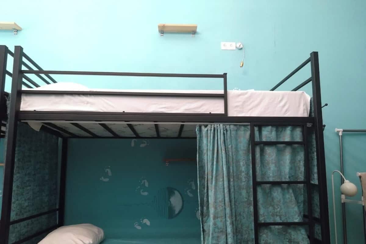 A bunk bed room with a blue wall, a small shelf, and a window with curtains.