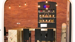 A bar area with a brick wall, hanging light bulbs, shelves with bottles, and black chairs. - Moosica Hostel (Tbilisi)