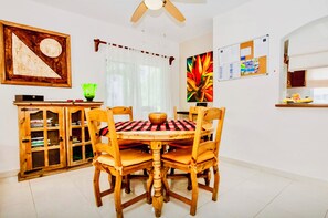 A dining area with a wooden table and chairs, a ceiling fan, a bulletin board, and a cabinet with glass doors.