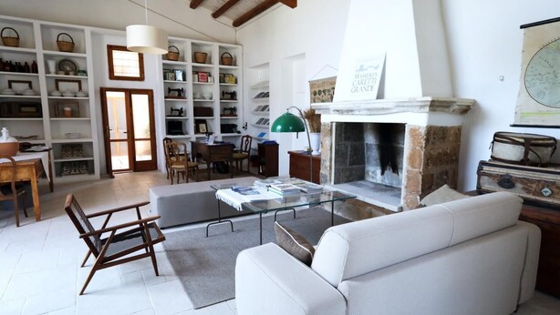 A spacious living room with a fireplace, a dining area with a table and chairs, and a bookshelf filled with various items. - Masseria Caretti Grande (Lecce)