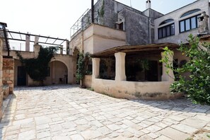 Ein Innenhof mit Steinpflaster, einer überdachten Sitzgelegenheit und einem Gebäude mit Balkon.