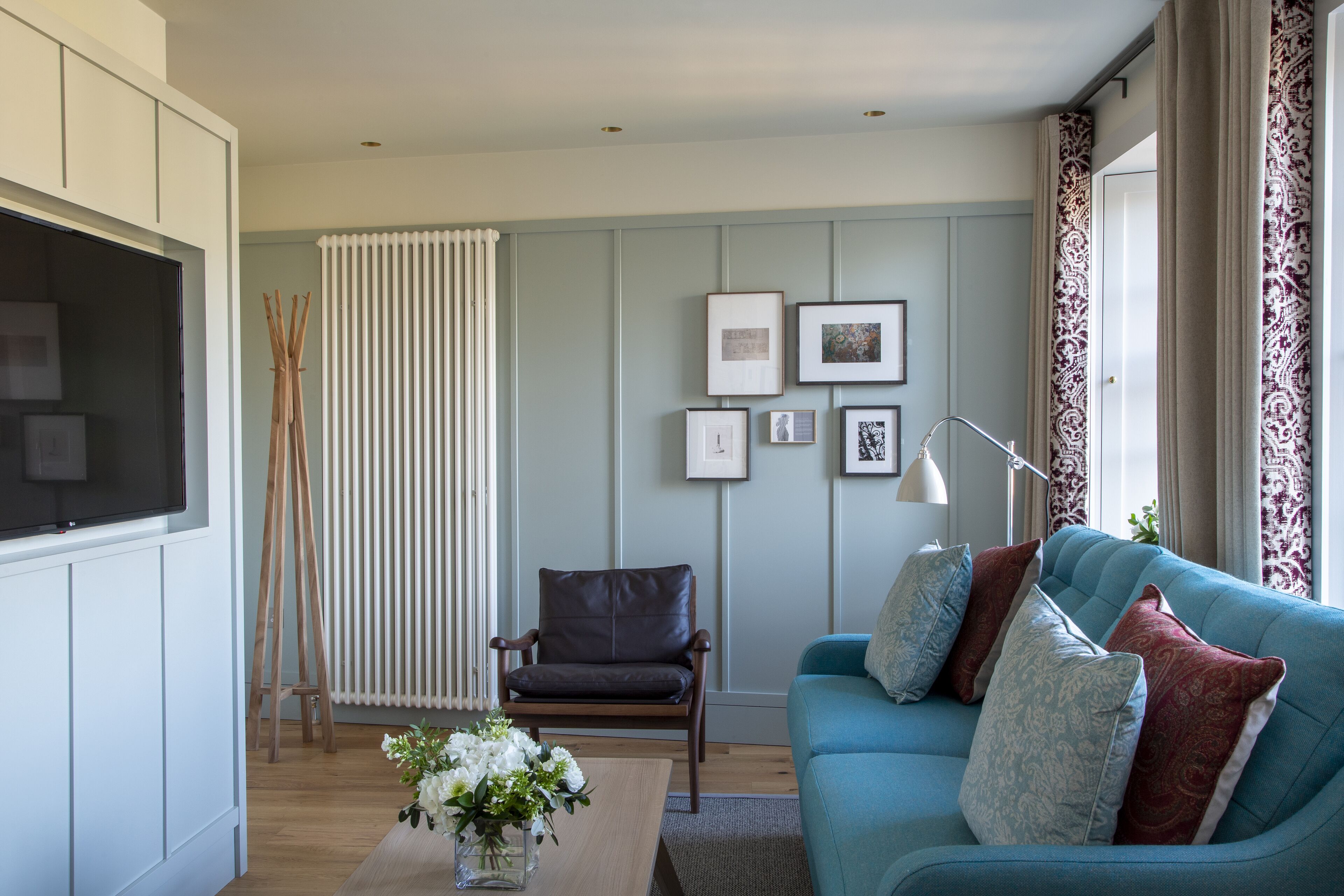 A modern living room with a blue sofa, a wooden chair, a white radiator, and framed pictures on the wall.