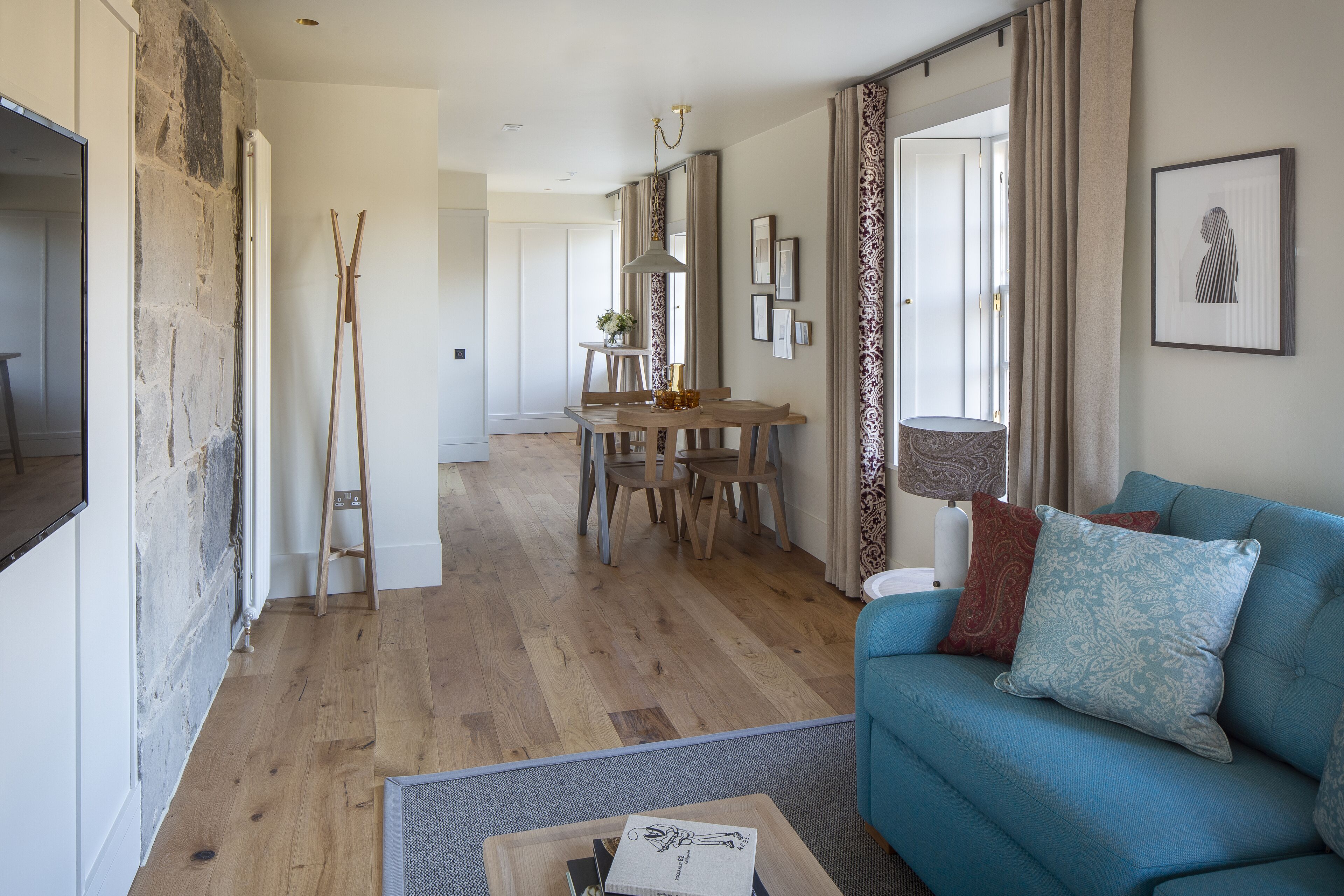 A modern living room with a blue sofa, wooden dining table, and a stone accent wall.