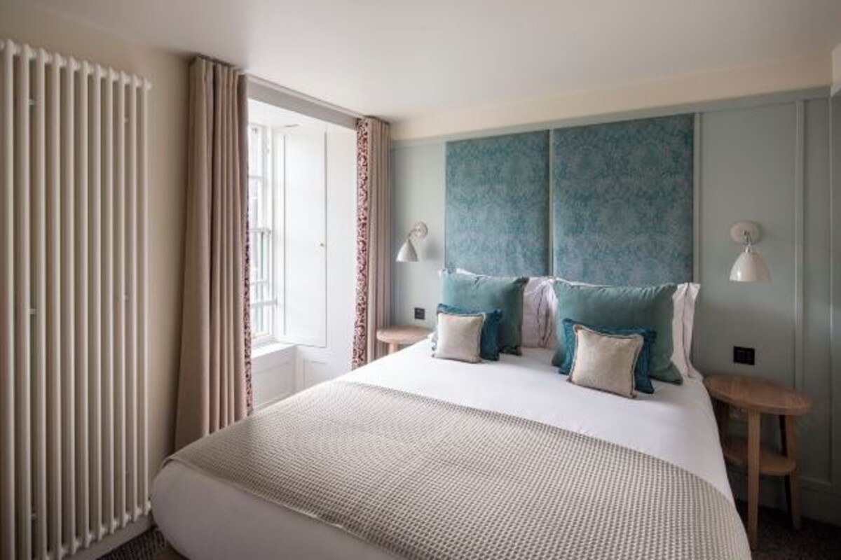 A hotel room with a large bed, a headboard with a textured design, two bedside tables with lamps, and a window with curtains.