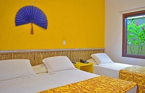 Habitación de hotel con dos camas, una pared amarilla, un ventilador colgante y una ventana con vista a la vegetación.