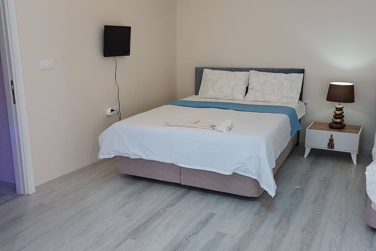 A bedroom with a bed, bedside table, lamp, and a mounted TV.