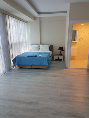 Un dormitorio con una cama, una mesita de noche y un baño visible a través de una puerta abierta.