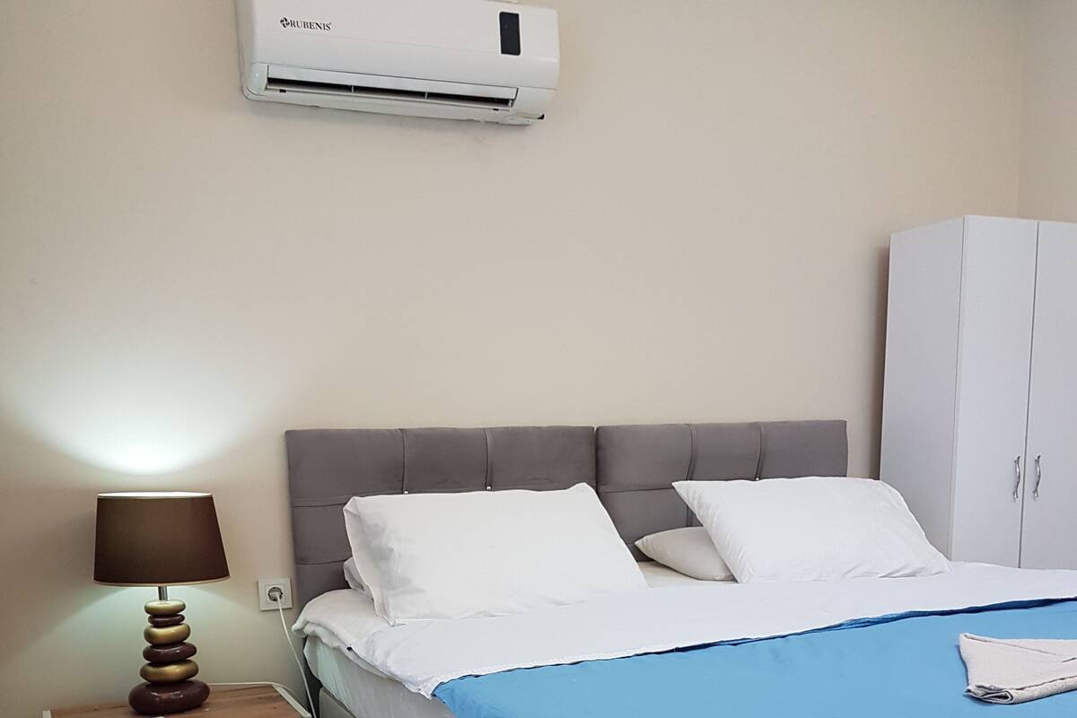 A bedroom with a bed, a nightstand, a lamp, an air conditioner, and a wardrobe.
