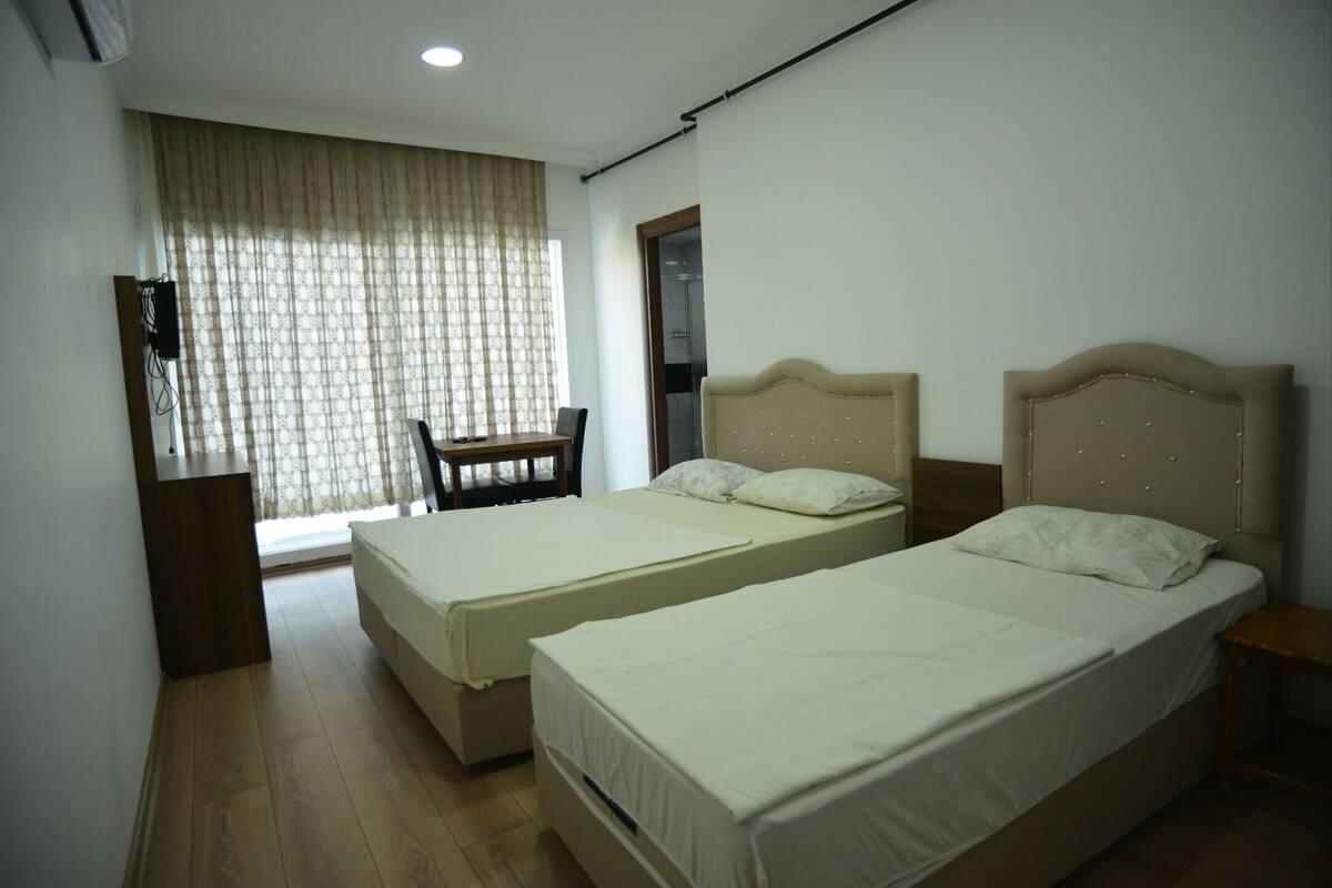 A room with two beds, a chair, a desk, and a window with curtains.