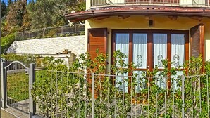 A two-story building with a balcony, a stone wall, and a metal fence with greenery. - La Quiete 17 Holideal (Tremosine)