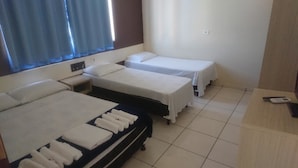 Quarto de hotel com duas camas de solteiro, uma pequena mesa de cabeceira com abajur e uma escrivaninha com telefone.