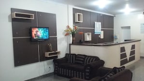 Uma área de recepção com televisão de tela plana na parede, balcão de recepção, sofá e um vaso com flores.