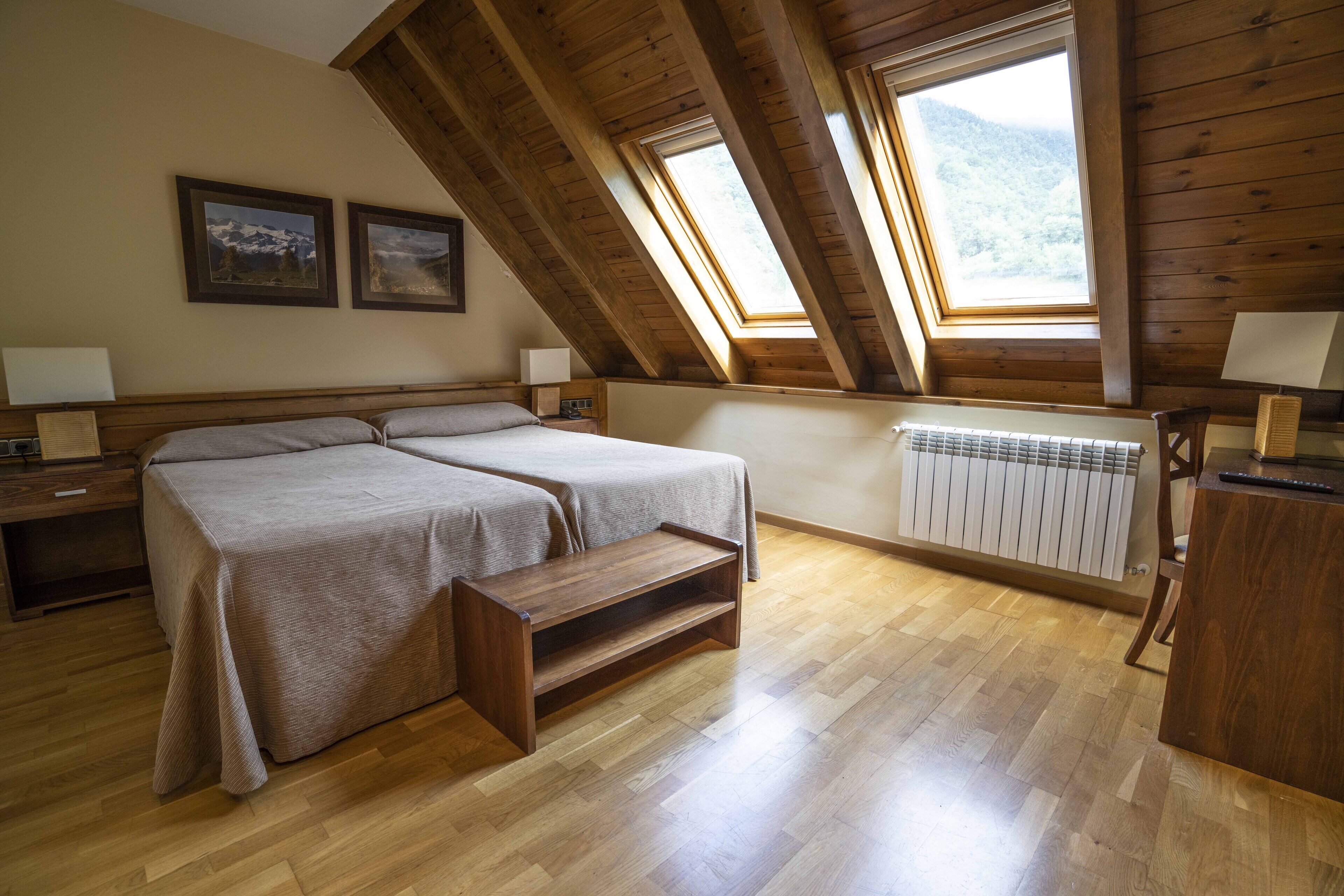 A bedroom with two beds, wooden flooring, a radiator, and a skylight.