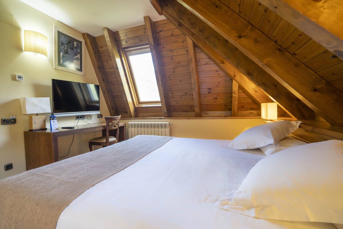 A room with a bed, a desk with a computer, a TV, and a window with a view of the sky.
