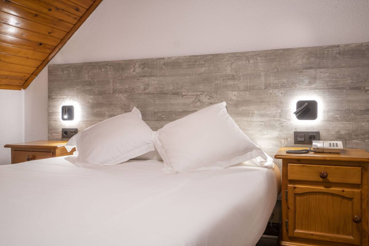 A bedroom with a wooden headboard, two bedside tables with lamps, a bed with white bedding, and a nightstand with a clock.