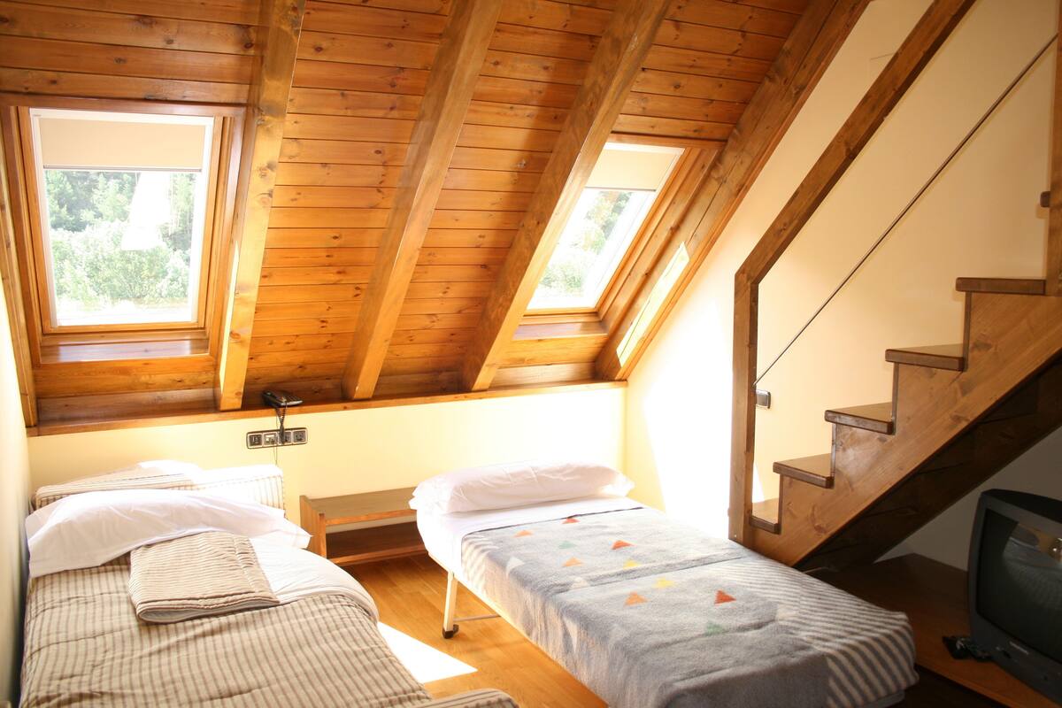 A bedroom with two single beds, wooden beams, a wooden staircase, and a television.