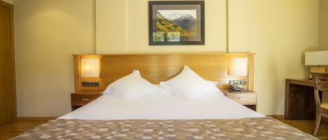 A hotel room with a large bed, wooden headboard, two bedside tables with lamps, a desk, and a chair.