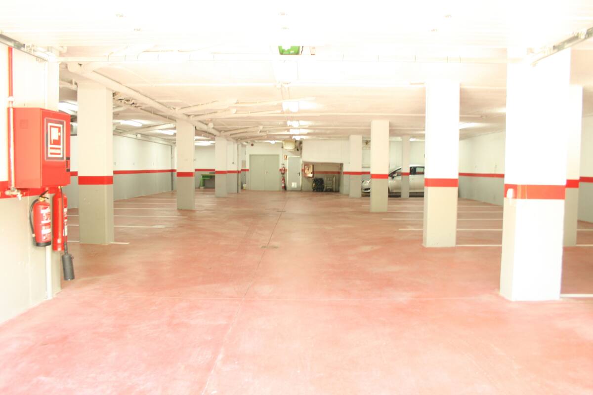 A multi-level parking garage with red and white pillars, a fire extinguisher, and a visible exit door.