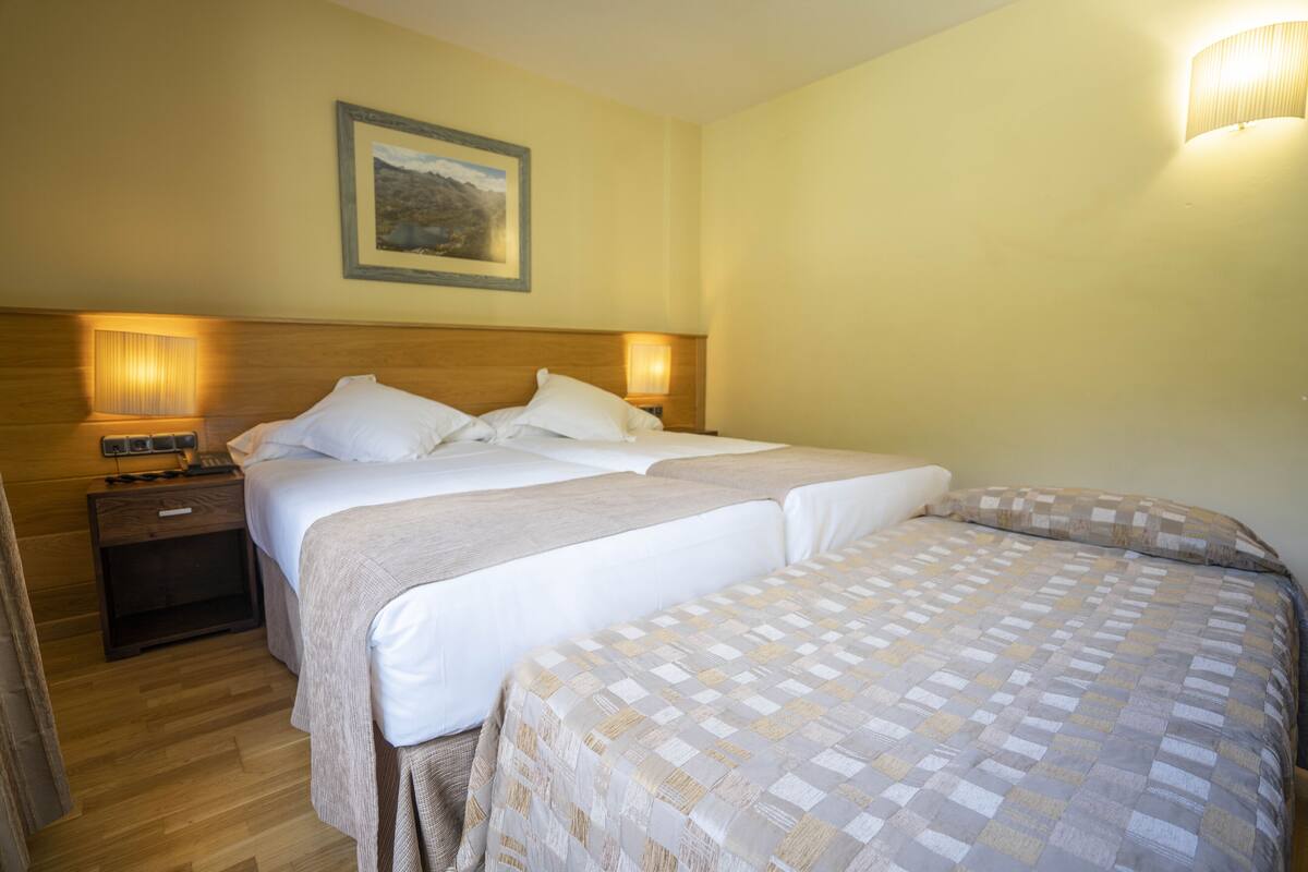 A hotel room with two beds, wooden headboard, bedside lamps, a nightstand, and a framed picture on the wall.