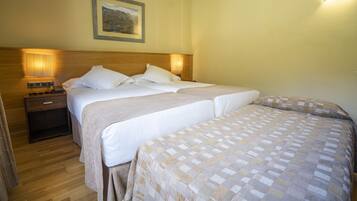 A hotel room with two beds, wooden headboard, bedside lamps, a nightstand, and a framed picture on the wall.