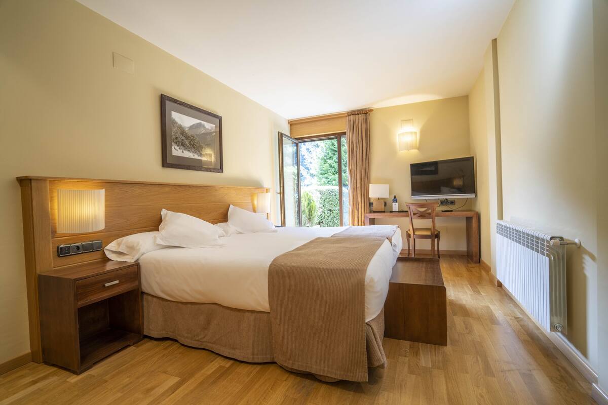 A hotel room with a large bed, a desk with a chair, a television, and a window with curtains.