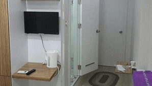 Ein Hotelzimmer mit einem Holzkasten, einem an der Wand befestigten Fernseher, einem kleinen Tisch mit Fernbedienung und einer weißen Tasse sowie einer Tür mit Glasschiebeelement.