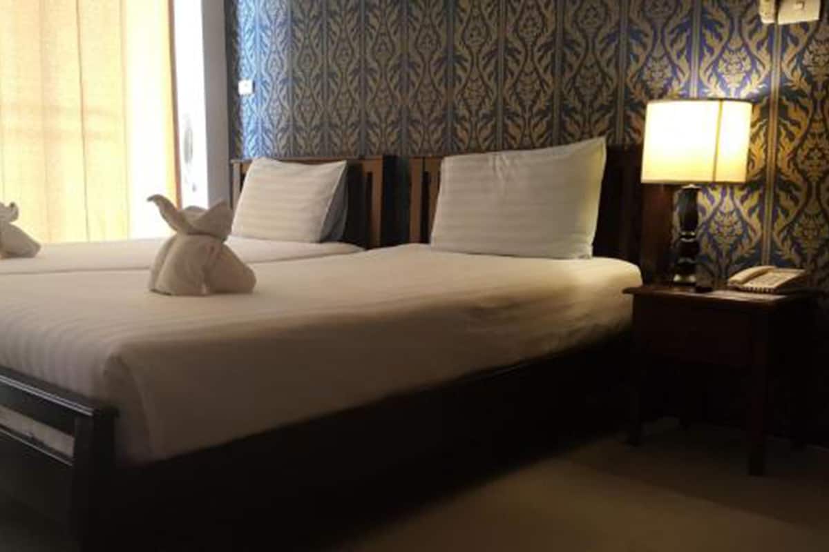 Una habitación de hotel con dos camas, una mesita de noche con lámpara y un papel tapiz estampado.