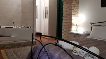 Una camera da letto con un letto, un comodino, una lampada, un bagno con una vasca e un muro in pietra.