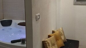 A spa room with a massage table, two cushions, a small glass, and a hot tub. - The Good Place (Cagliari)
