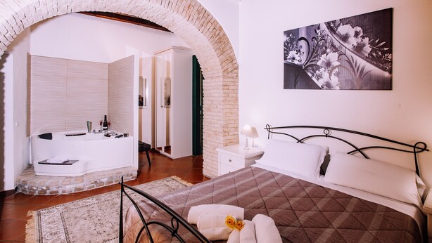 A bedroom with a large bed, a bathroom with a bathtub, and a brick archway. - The Good Place (Cagliari)