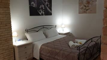 Una cama bien hecha con un colcha marrón, dos mesitas de noche con lámparas, y una pared decorada con motivos florales.
