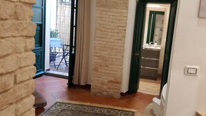 A hallway with a brick wall, a patterned rug, and a door leading to a bathroom with a mirror and a sink. - The Good Place (Cagliari)