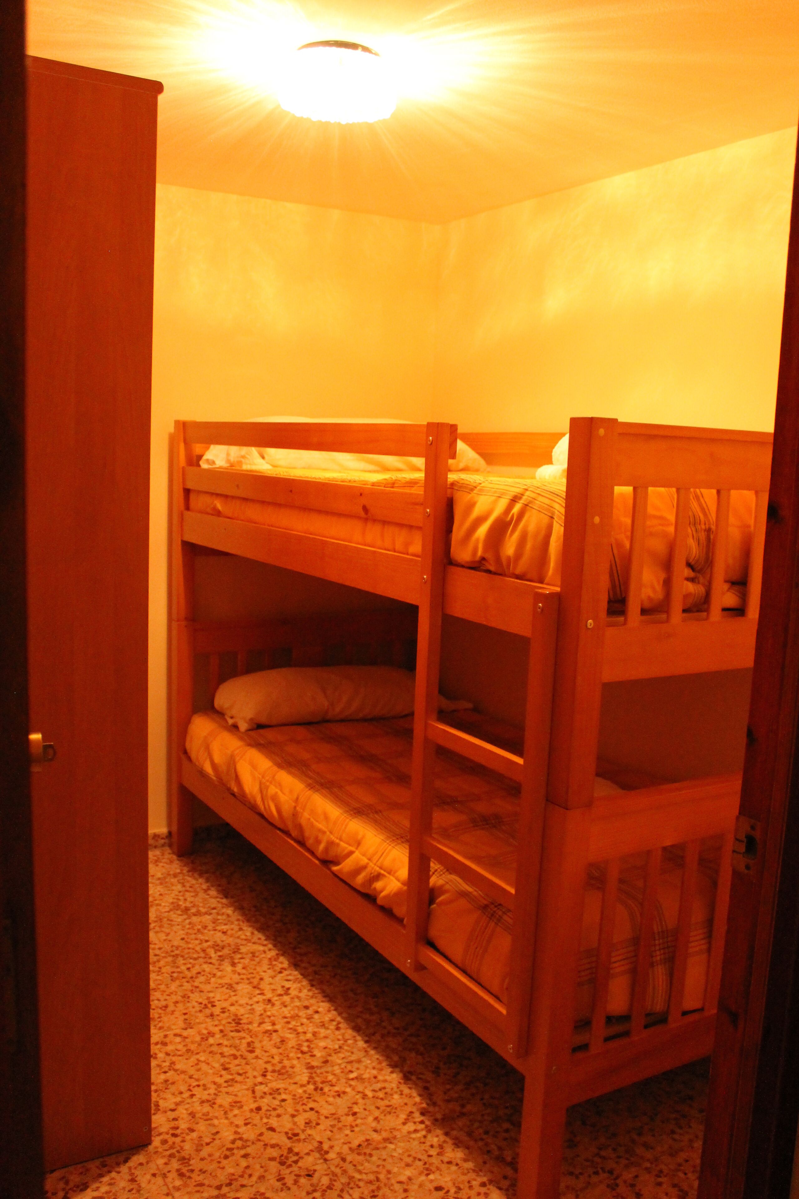 Una cama litera en una habitación con suelo alfombrado y una puerta a la izquierda.