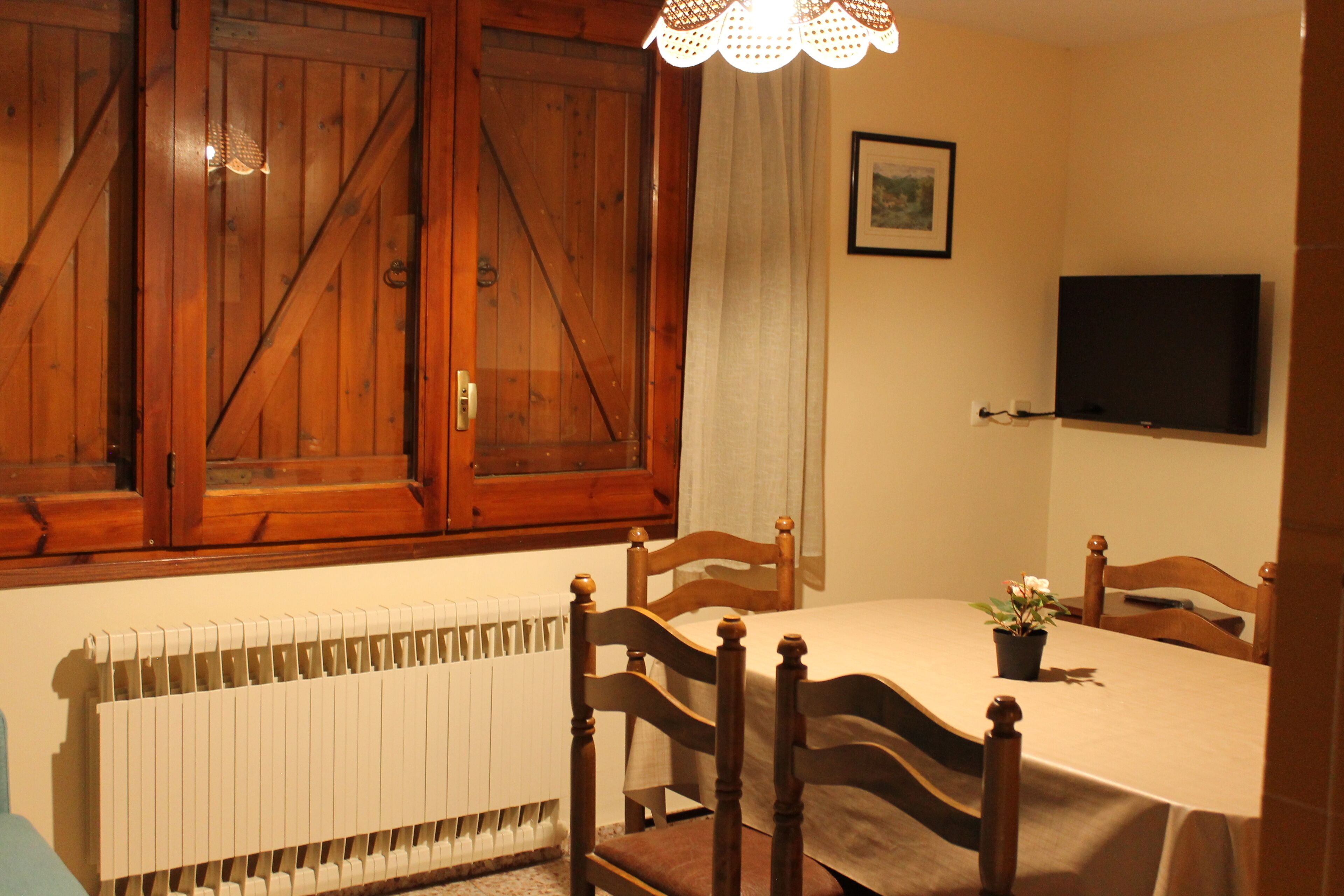Un coin repas comprenant une table, des chaises, un radiateur, un téléviseur et des meubles de rangement en bois.