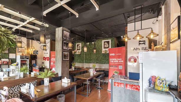 A modern hotel lobby with wooden tables, comfortable seating, and a green wall with framed pictures. - OYO 685 Am Bed Hostel (Bangkok)