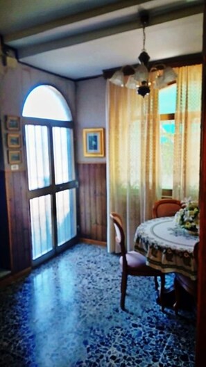 A room with a large window, a dining table with chairs, and a ceiling fan. - Privacy & Relax in Sardegna (Alghero)