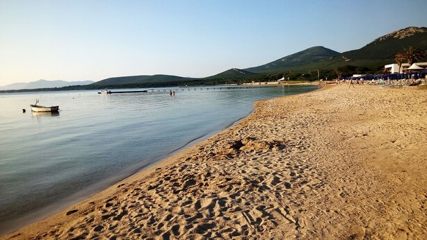 A beach with a boat in the water, a sandy shore, and mountains in the background. - Privacy & Relax in Sardegna (Alghero)