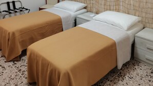 A hotel room with two single beds, a small table, a chair, a bedside table, a wall-mounted air conditioner, and a picture frame on the wall. - Privacy & Relax in Sardegna (Alghero)