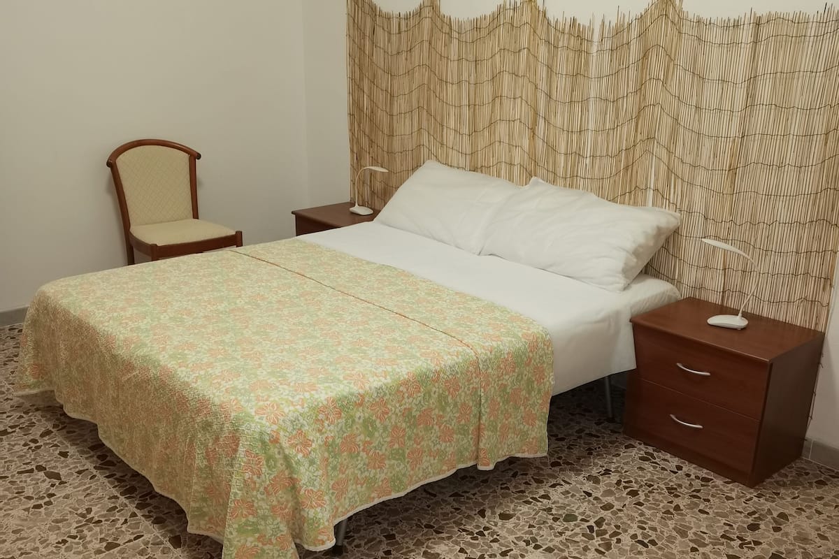 A bedroom with a bed, nightstands, a chair, and a patterned floor.